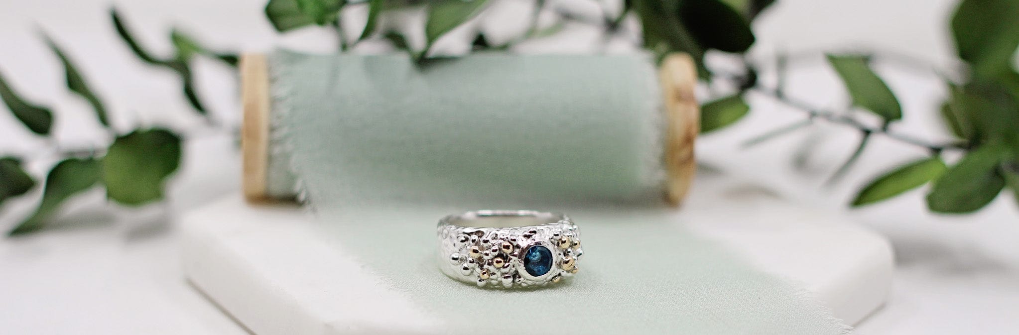 Silver ring with a blue gemstone on a white surface with greenery in the background