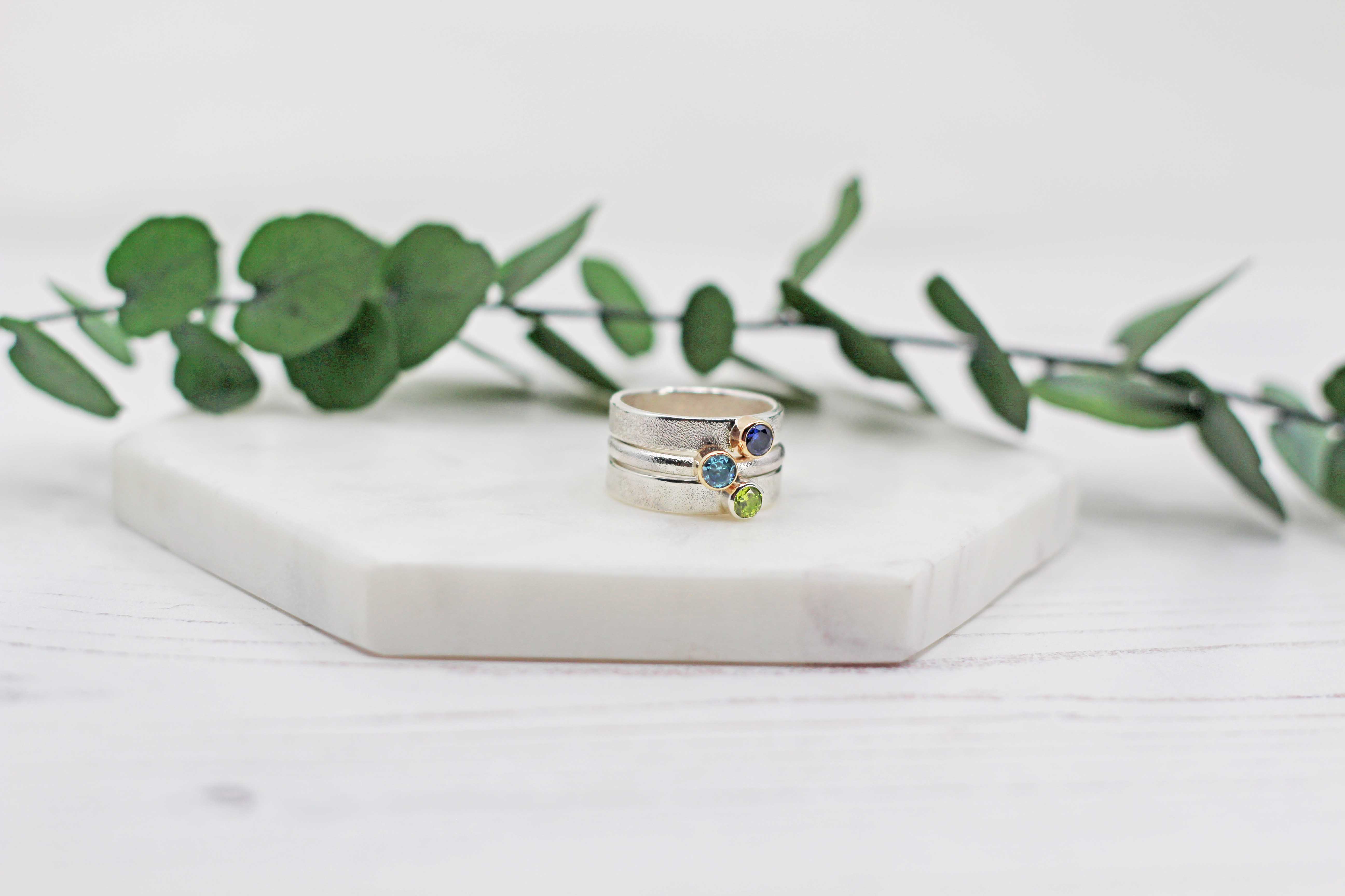 Silver ring with colorful stones on a white surface with green leaves